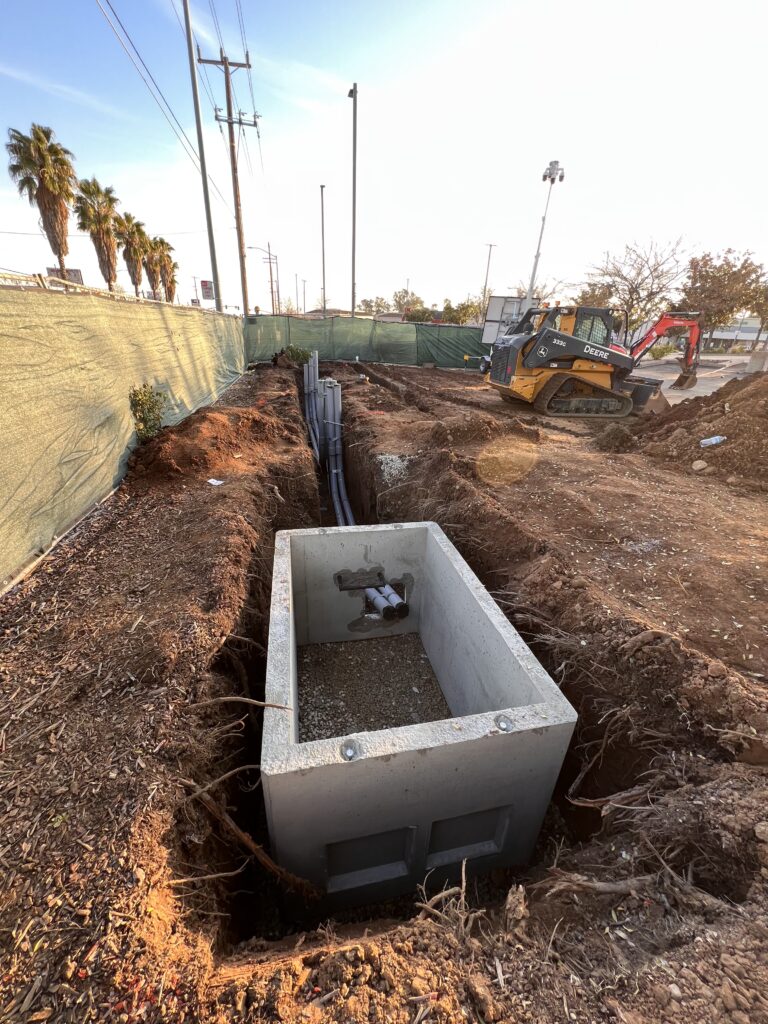 construction site with electrical cords running to a vault. With a Deer mini excavator in the background on the right side.