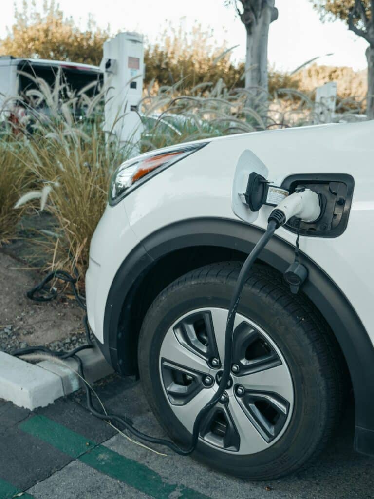 A white charger handle plugged into the front of a white car with desert landscape in the background